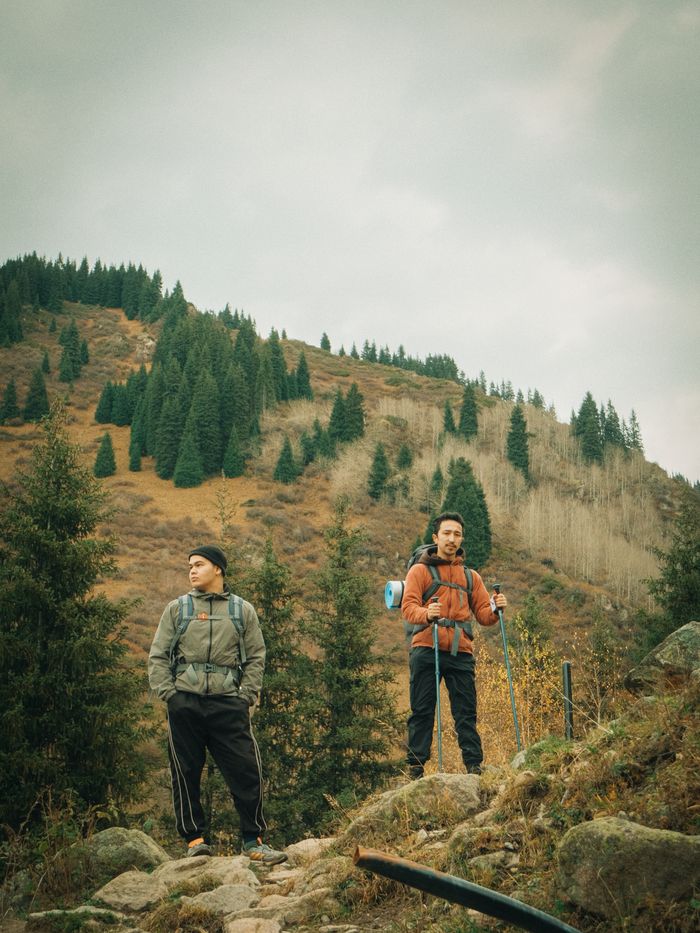 Services Two hikers with backpacks standing on a scenic mountain trail surrounded by evergreen trees.